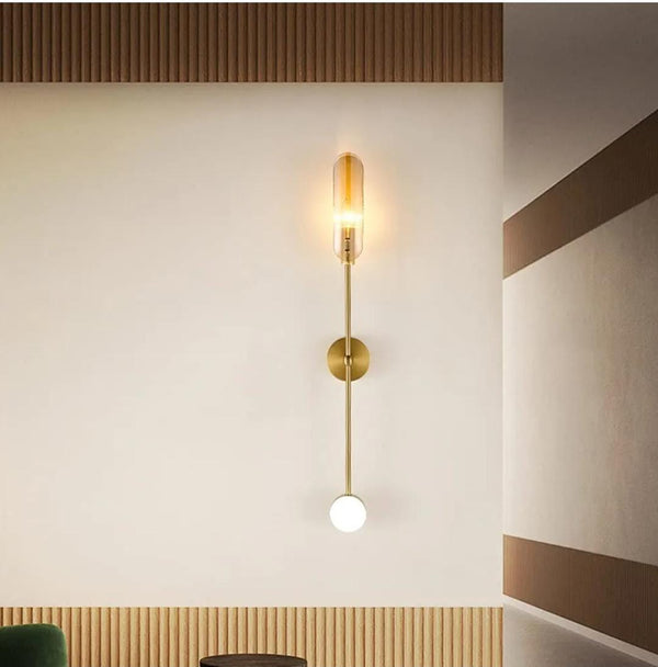 Vertical brass wall sconce with amber glass capsule top and frosted globe bottom creating a modern layered double light effect.