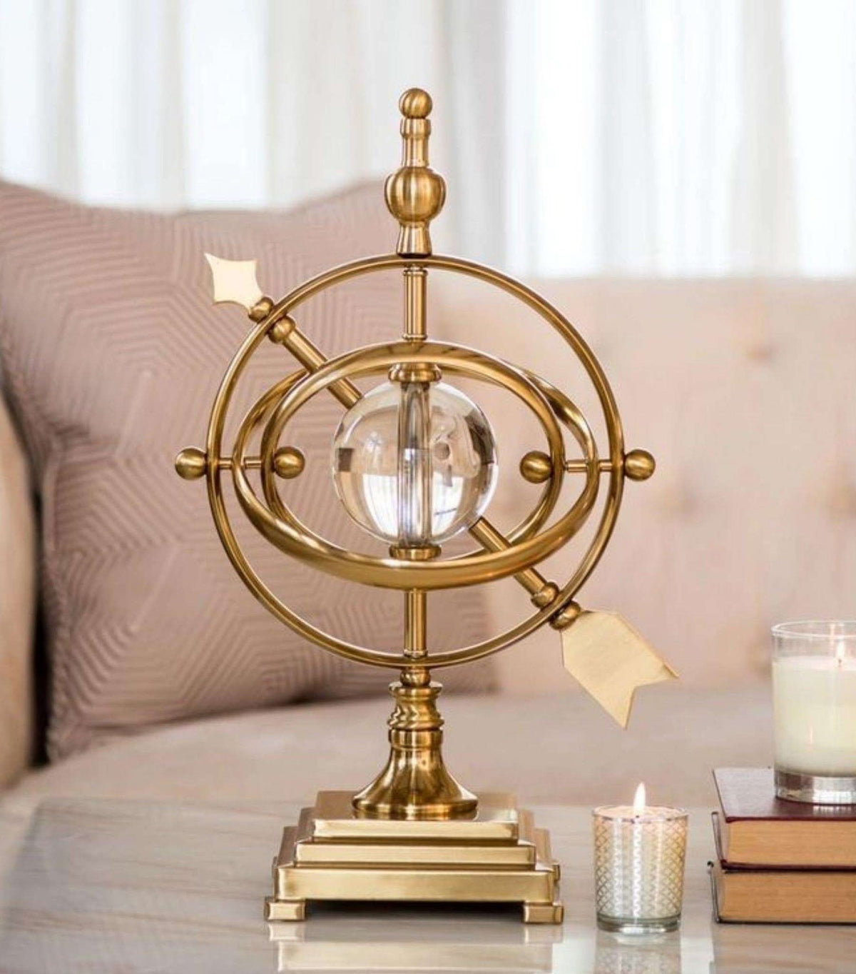 Gemelli Collections gold armillary sphere sculpture with rotating metal rings and clear crystal ball centre mounted on a tiered gold display base.