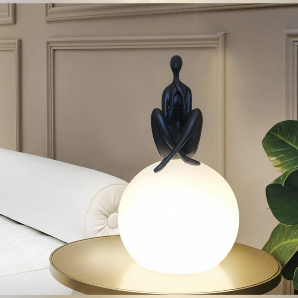Gemelli Collections Zen yoga sculpture globe lamp featuring a matte black meditating figure seated on a glowing white LED globe, modern decorative table light for living rooms, bedrooms, offices, and wellness spaces.