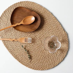 Oval woven placemat for dining table settings, providing a practical protective surface for plates, bowls, cups, and decorative table arrangements