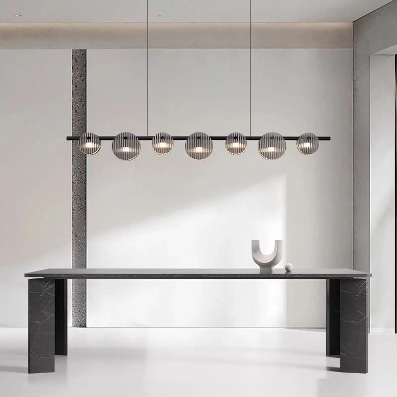 Matte black linear chandelier with seven smoked ribbed glass discs emitting soft diffused warm LED light in a minimalist horizontal design.