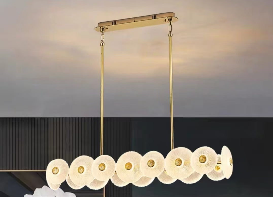 Gold linear chandelier with overlapping frosted petal discs and integrated LED lighting creating a soft organic contemporary glow.