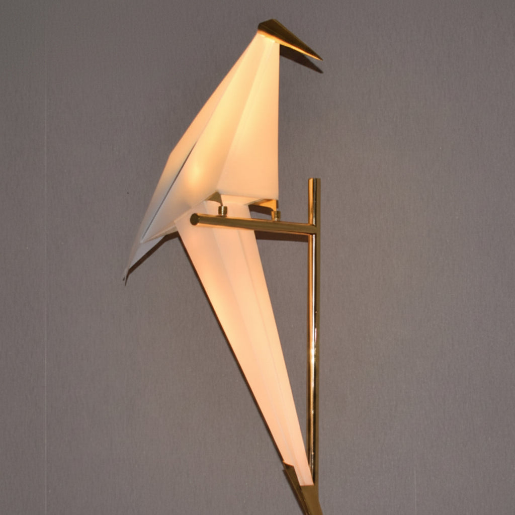 Gemelli Collections geometric origami bird floor lamp featuring a glowing white acrylic bird mounted on a polished gold stand, modern sculptural LED lighting for living rooms, bedrooms, hotels, offices, and luxury interiors.